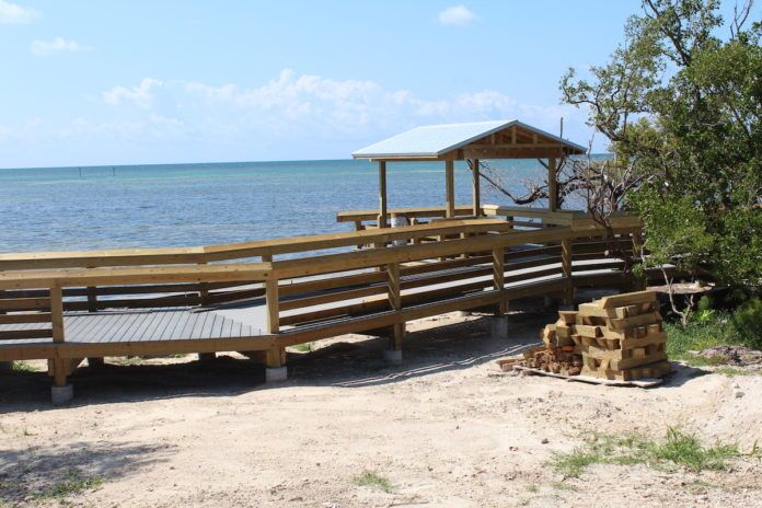 0822AnnesBeach Anne’s Beach reopens following damage sustained from Irma - A wooden bench sitting on top of a sandy beach - Anne's Beach