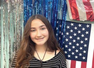 STUDENT SPOTLIGHT: TVM’S OLIVIA ZISCHKA a girl standing in front of a wall with american flags