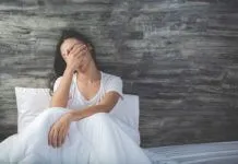 a woman sitting on a bed covering her eyes