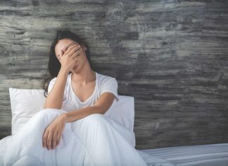 a woman sitting on a bed covering her eyes