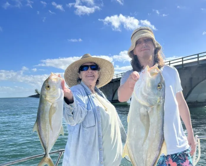 a couple of women standing on top of a boat holding fish