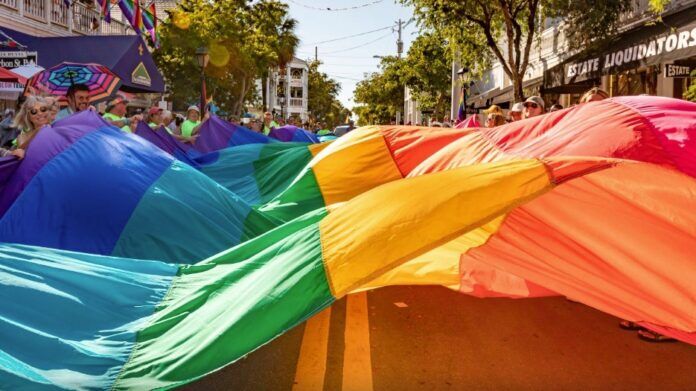 a group of people walking down a street holding a rainbow colored umbrella