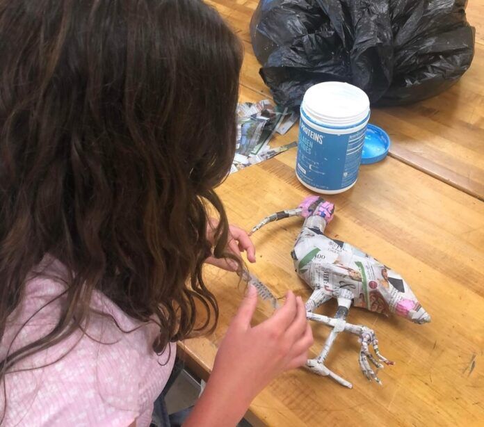 a young girl sitting at a table making a paper dragon