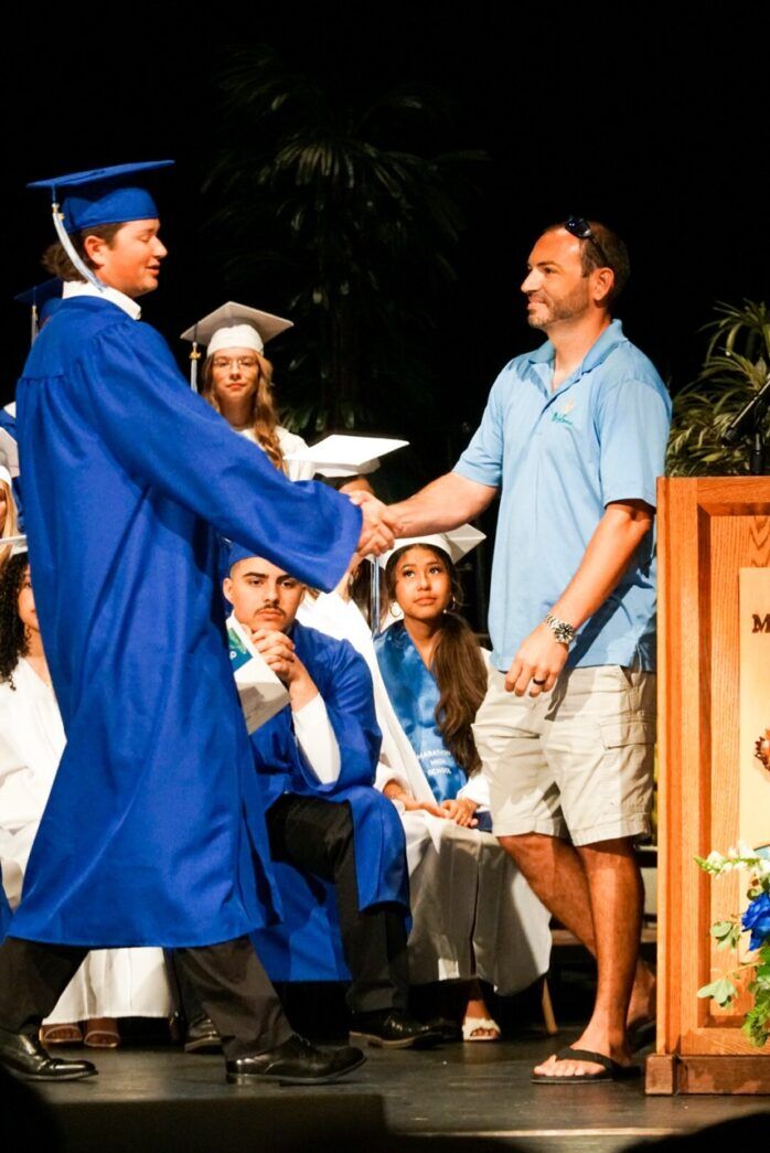 a man in a blue graduation gown shaking hands with a man in a blue cap