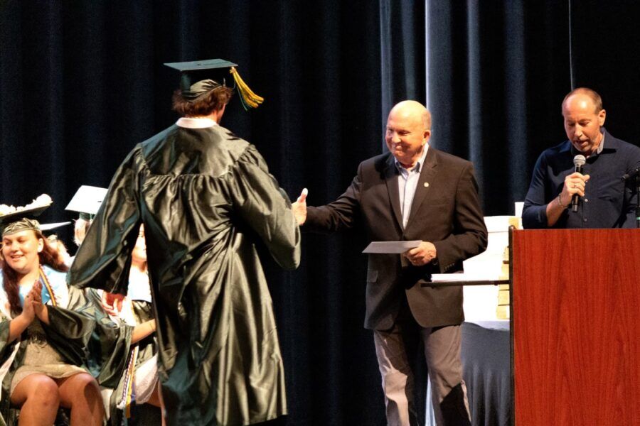 a man in a graduation cap and gown speaking at a podium