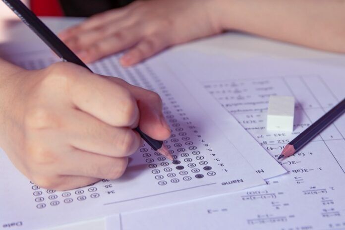Students hand holding pencil writing selected choice on answer sheets and Mathematics question sheets. students testing doing examination. school exam a person writing on a piece of paper with a pencil