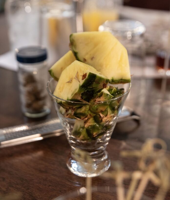 Pineapple wedges a glass filled with fruit on top of a wooden table