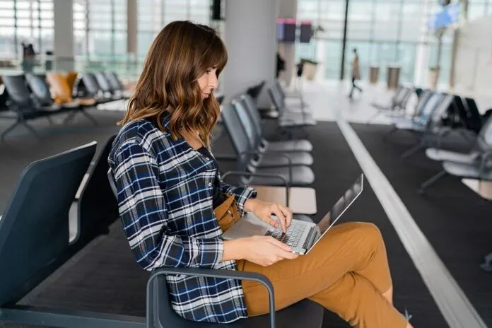 Airport Young female passenger with laptop sitting in terminal hall while waiting for her flight
