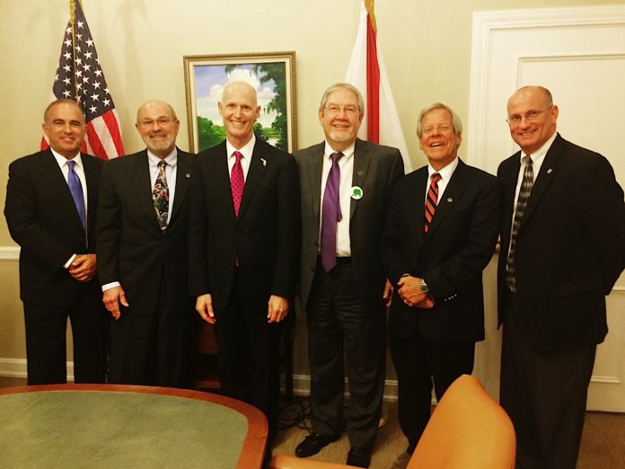 Rick Scott et al. standing next to a person in a suit and tie - Businessperson