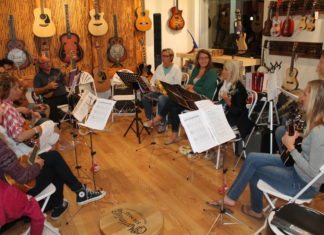 Learn how to play the ‘uke’ and be in a band - A group of people sitting at a table - Cello