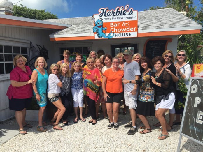 Foodies visit Herbie’s – Local group indulges in monthly tastings - Francoise Pascal et al. standing in front of a crowd posing for the camera - Duck Key