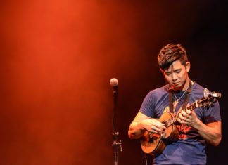 The Lord of the (4) Strings The Lord of the (4) Strings - Jake Shimabukuro standing on a stage holding a guitar - Jake Shimabukuro