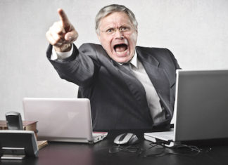 Top ways to make your boss angry - A person sitting at a desk with a laptop and smiling at the camera - Leadership