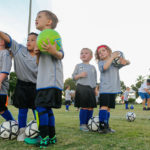 PRACTICE MAKES THE PLAYER - A group of young children standing next to a football ball - Team