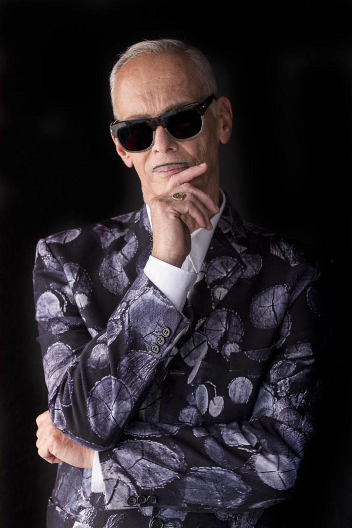 John Waters is Coming to Town… an Interview with the Icon - A man wearing glasses talking on a cell phone - Make Trouble