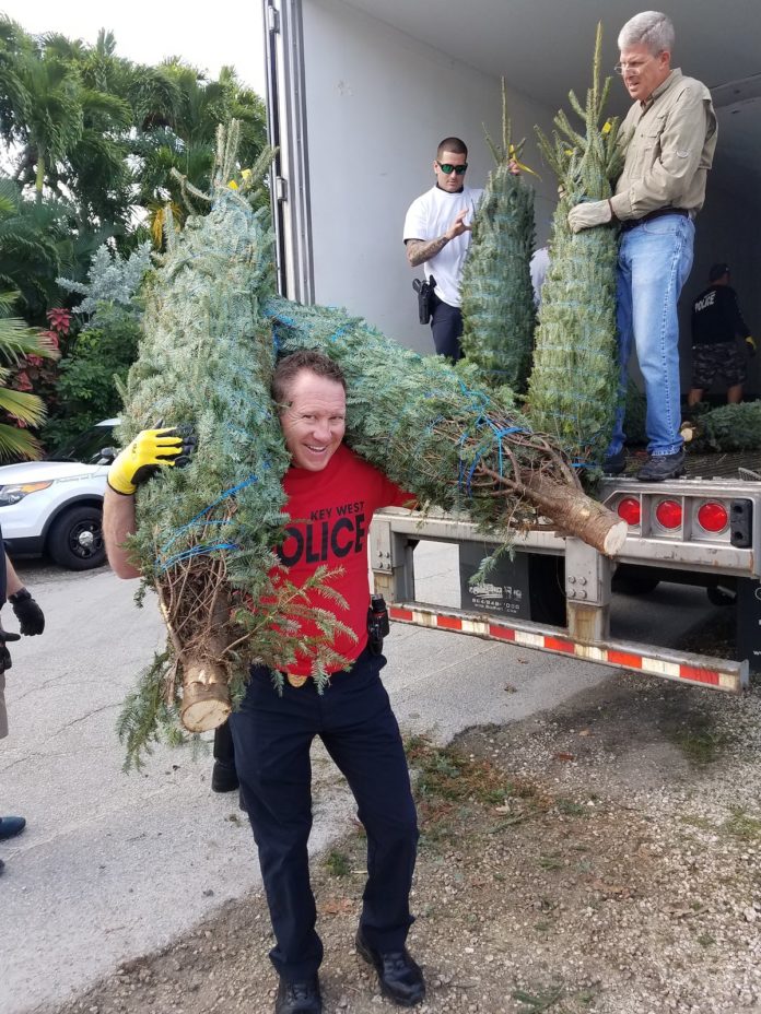 Key West Police Officer Joe Tripp totes two Christmas trees, as Officer Alex Rodriguez and Sunrise Rotarian Jim Scholl continue doling them out to a line of volunteers. MANDY MILES/Keys Weekly