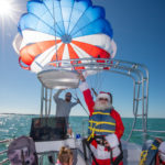 GLIDING INTO SEASON LIKE … - A group of people on a beach - Parasailing