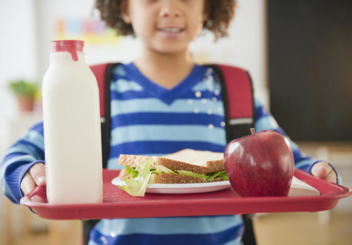 School lunch debts linger – Principal corrects superintendent’s claims - A small child sitting on a table - Cafeteria