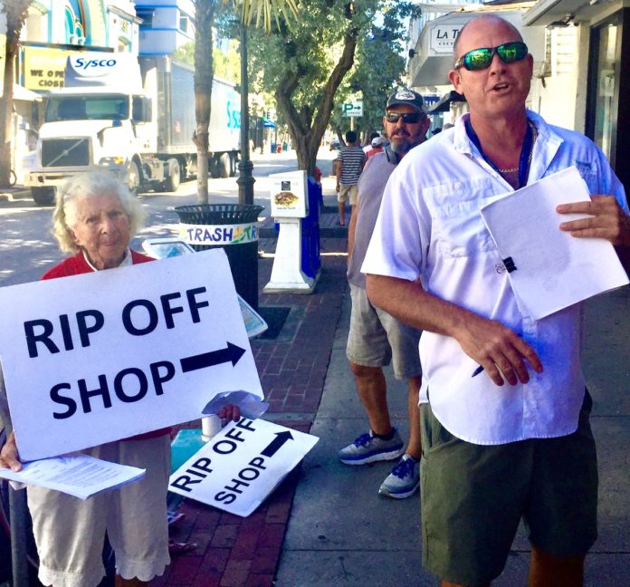 A typical picketing protest in front of Orogold cosmetic shop on Duval Street accuses the shop’s owners and employees of unethical business practices.MANDY MILES/’The Weekly Top: Orogold cosmetic shop owner Nir Chen sued Shirlee Ezmirly, a 92-year-old volunteer protester with the Key West Rip-Off Rapid Response Team, and 14 other team members who regularly picket the shop. KEY WEST RIP-OFF RAPID RESPONSE TEAM/Contributed Bottom: Shirlee Ezmirly, thumbs through a lawsuit, filed by Orogold shop owner that names Ezmirly and 14 other picketers as defendants in a defamation suit.