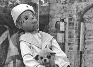 a creepy doll sitting in a chair holding a small dog