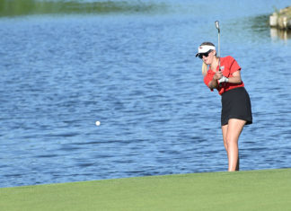 a woman in a red shirt and black skirt playing golf