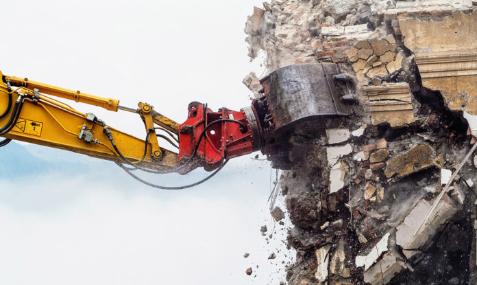 a yellow and red excavator digging through a large pile of rubble