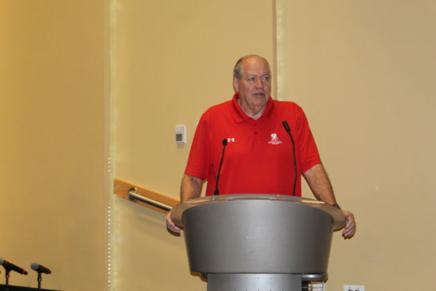 a man in a red shirt standing at a podium