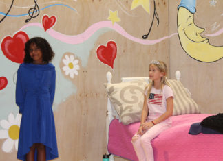 a woman standing in front of a bed next to a little girl