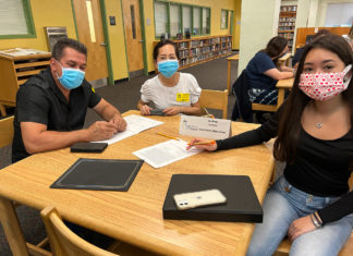 a group of people sitting at a table wearing face masks