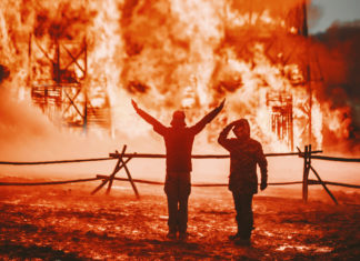 two people standing in front of a large fire