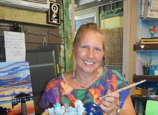 a woman sitting at a counter holding a paintbrush