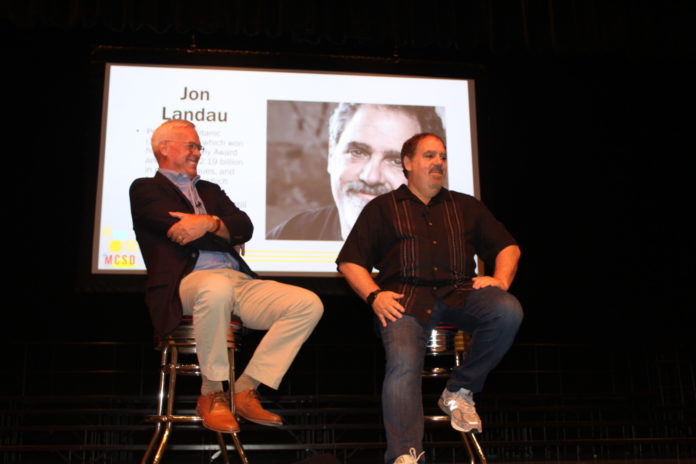 two men sitting on stools in front of a projector screen