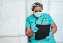 a woman in scrubs and a face mask holding a tablet