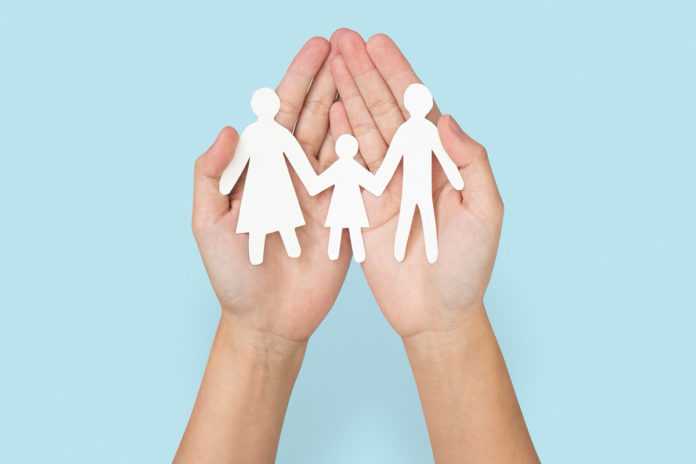 two hands holding a paper cutout of a family
