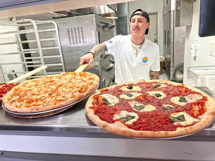 a man standing in front of two large pizzas