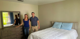 a man and woman standing in front of a bed in a bedroom