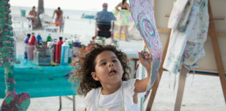 a little girl holding up a piece of art on the beach