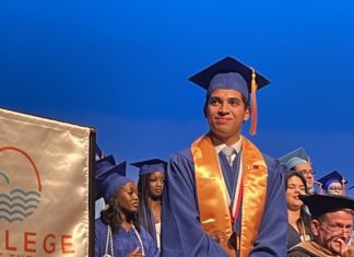 a man in a graduation cap and gown standing in front of a group of graduates