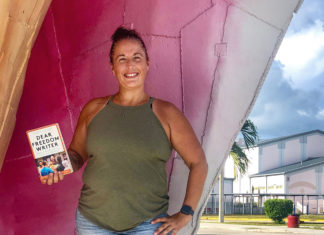 a woman standing in front of a pink wall holding a book