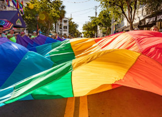 a group of people walking down a street holding rainbow colored umbrellas