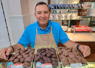 a man standing behind a counter filled with chocolates