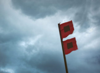 two red flags on a pole under a cloudy sky