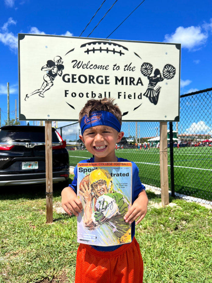 a young boy holding a football book in front of a sign