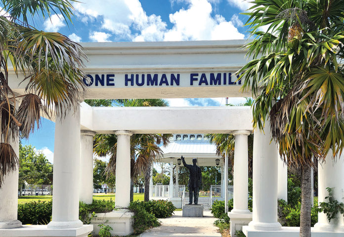 a statue of a man in a suit stands under a one human family sign