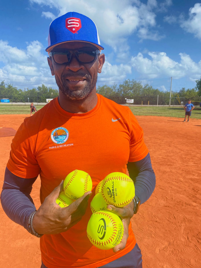 a man in an orange shirt and blue hat holding three yellow softballs