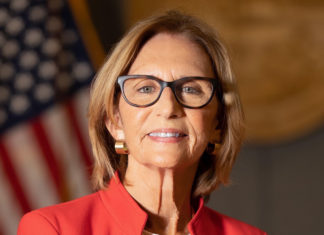 a woman in a red jacket and glasses standing in front of an american flag
