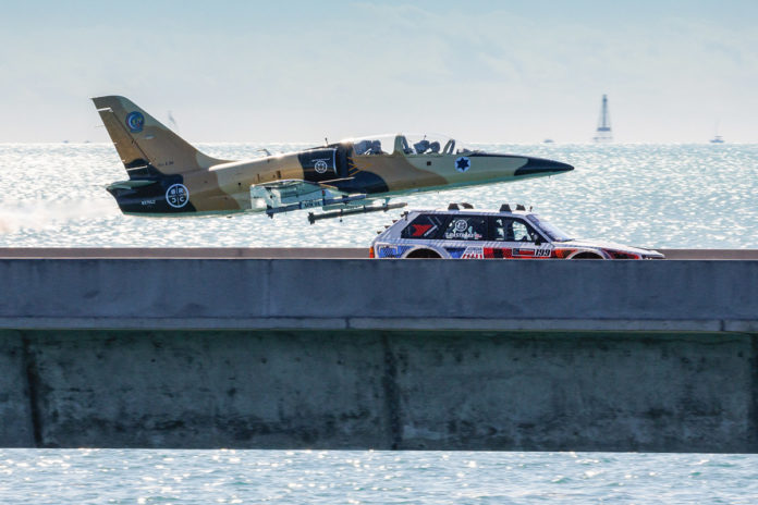 a plane flying over the ocean next to a car