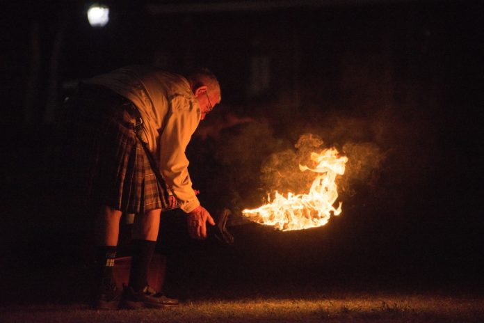 a man standing over a fire in the dark