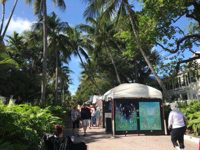 a group of people walking down a sidewalk next to palm trees