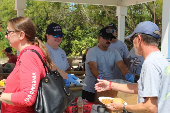 Firefighters hand out food Large a group of people standing around a table